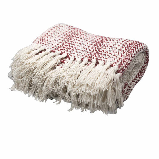 A red and white patterned throw blanket with long, off-white fringe lies rolled on a white background.