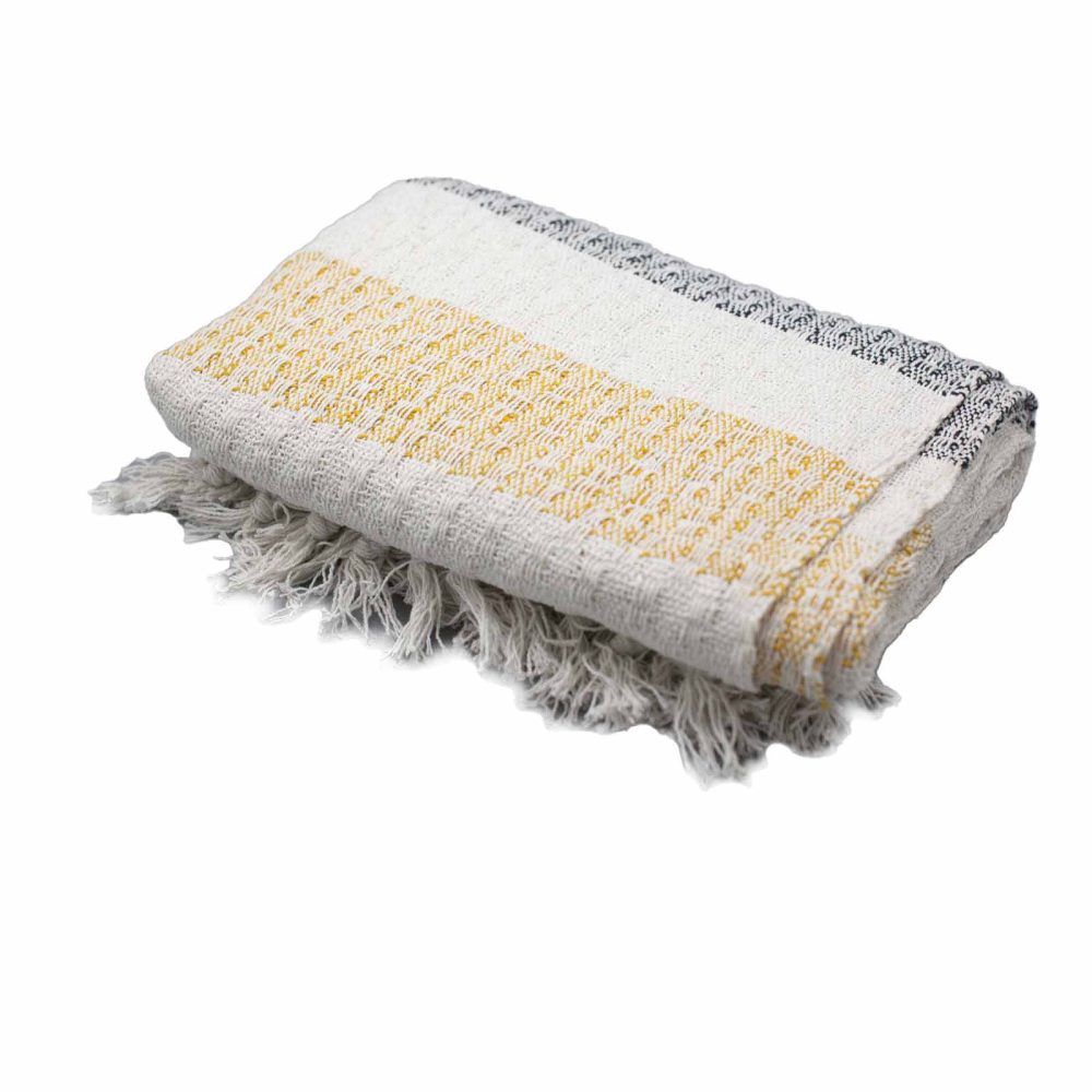 A woven throw blanket, folded, with off-white, mustard yellow, and grey stripes and frayed edges, rests on a white background.