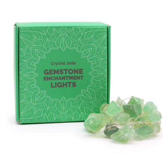 Gemstone lights sit near a green box labeled "Crystal Jade, GEMSTONE ENCHANTMENT LIGHTS" with a floral design on a white surface.