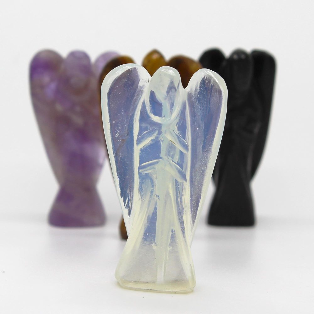 Crystal angels stand in a row on a white surface. The angel in front is opalescent; purple, brown, and black angels are behind it.