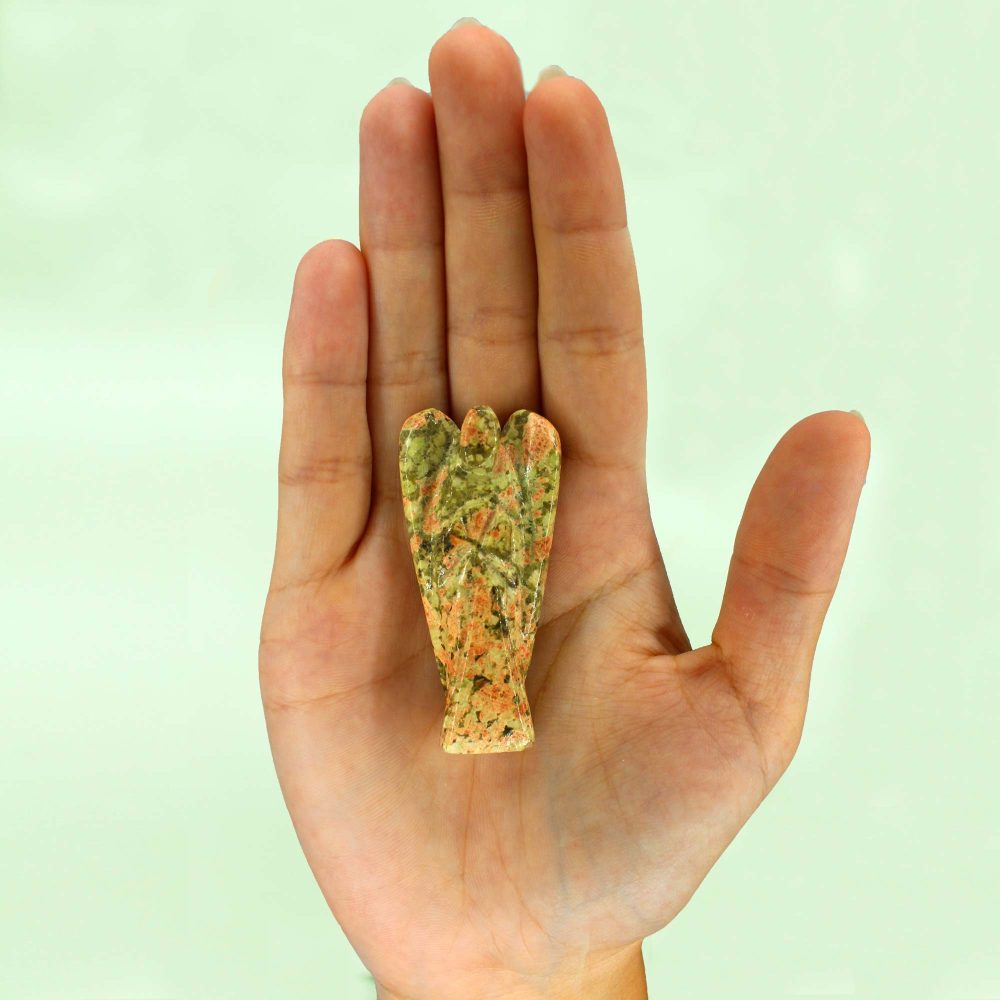 A small, stone angel with mottled green and orange coloring rests in the palm of a hand, against a solid, light green background.