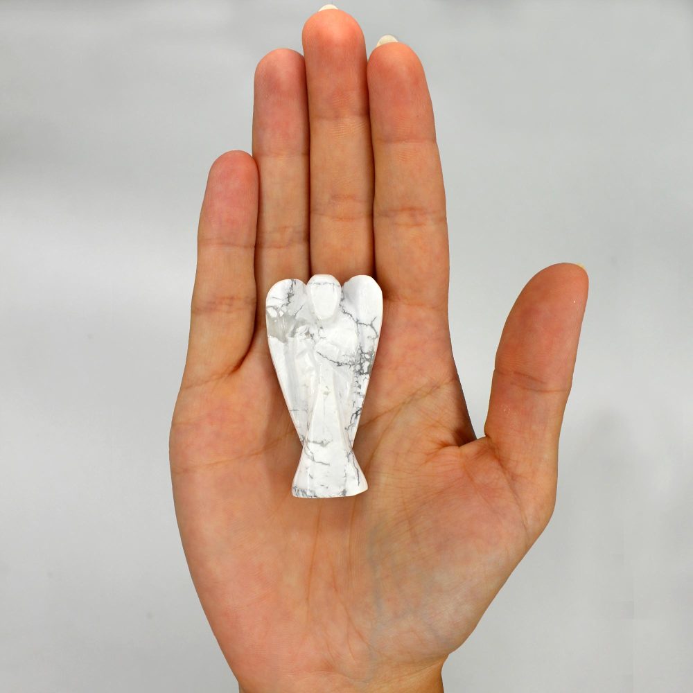 A small, white, stone angel figurine with gray marbling sits in the palm of an open hand. The background is a uniform white.