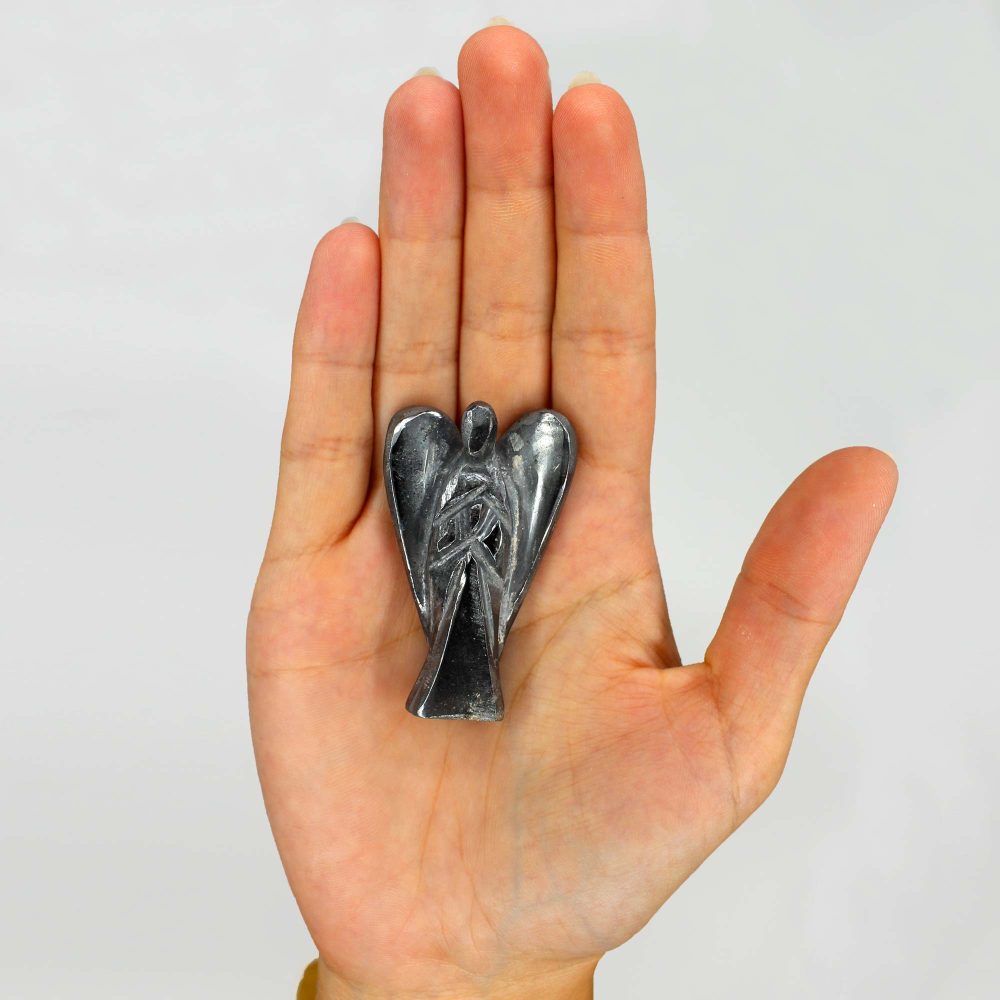 A small, gray angel figure rests in the palm of a hand. The background is plain and white.