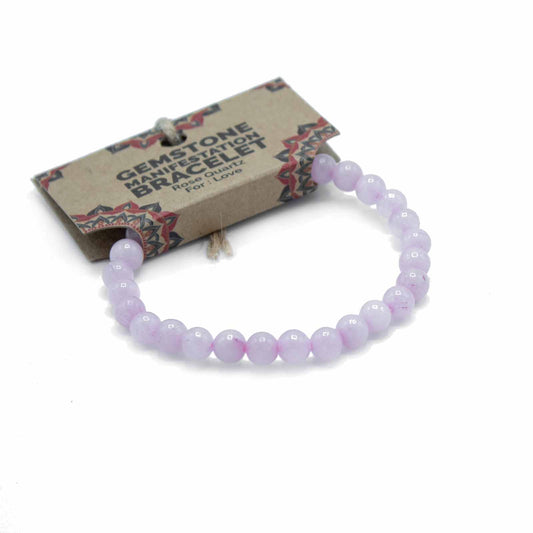 A light purple gemstone bracelet, made of round beads, rests on a white background; attached is a card reading “GEMSTONE MANIFESTATION BRACELET Rose Quartz For: Love”.