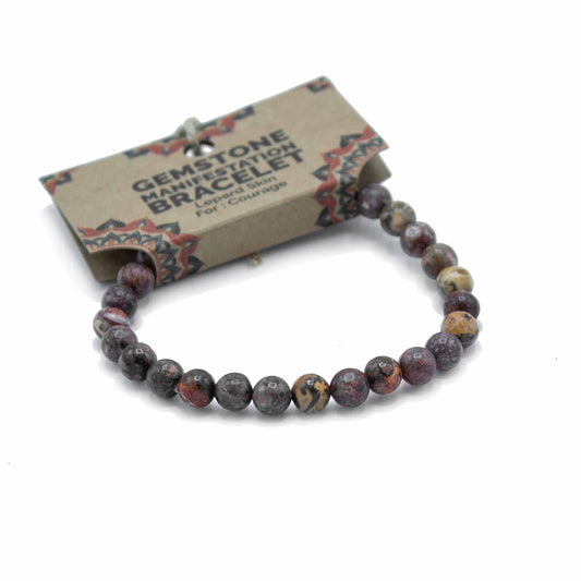 A gemstone bracelet rests on a white background. It is made of dark, mottled beads. The accompanying tag reads: GEMSTONE MANIFESTATION BRACELET Leopard Skin For: Courage.