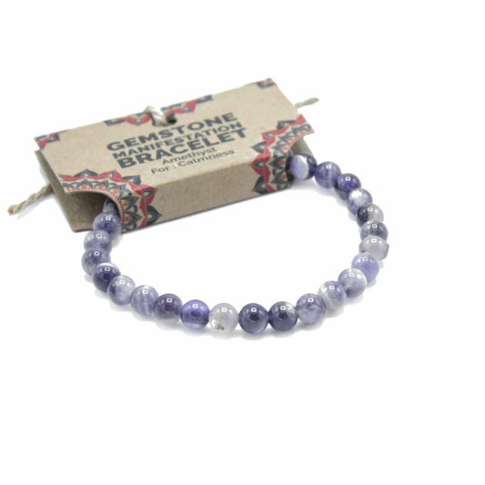 An amethyst gemstone bracelet rests on a white background; it is presented on a small, printed cardboard tag reading "GEMSTONE MANIFESTATION BRACELET Amethyst For Calmness".
