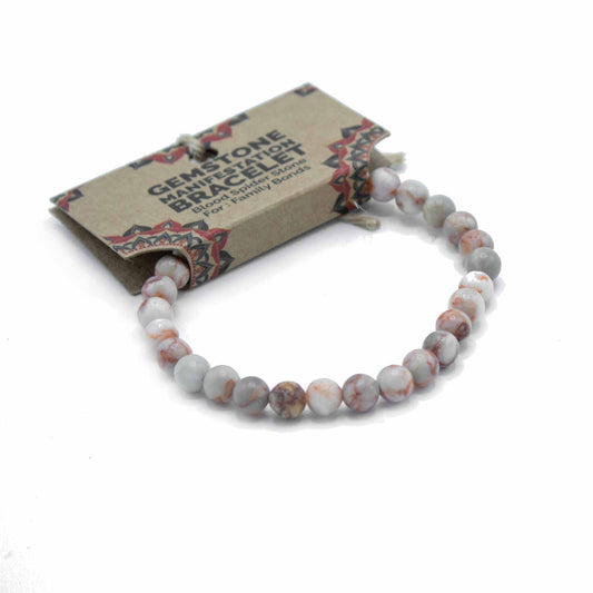 A gemstone manifestation bracelet, composed of light grey and reddish-brown marbled beads, rests on a white background, packaged in a kraft paper box with the words “GEMSTONE MANIFESTATION BRACELET Blood Spider Stone For: Family Bonds”.
