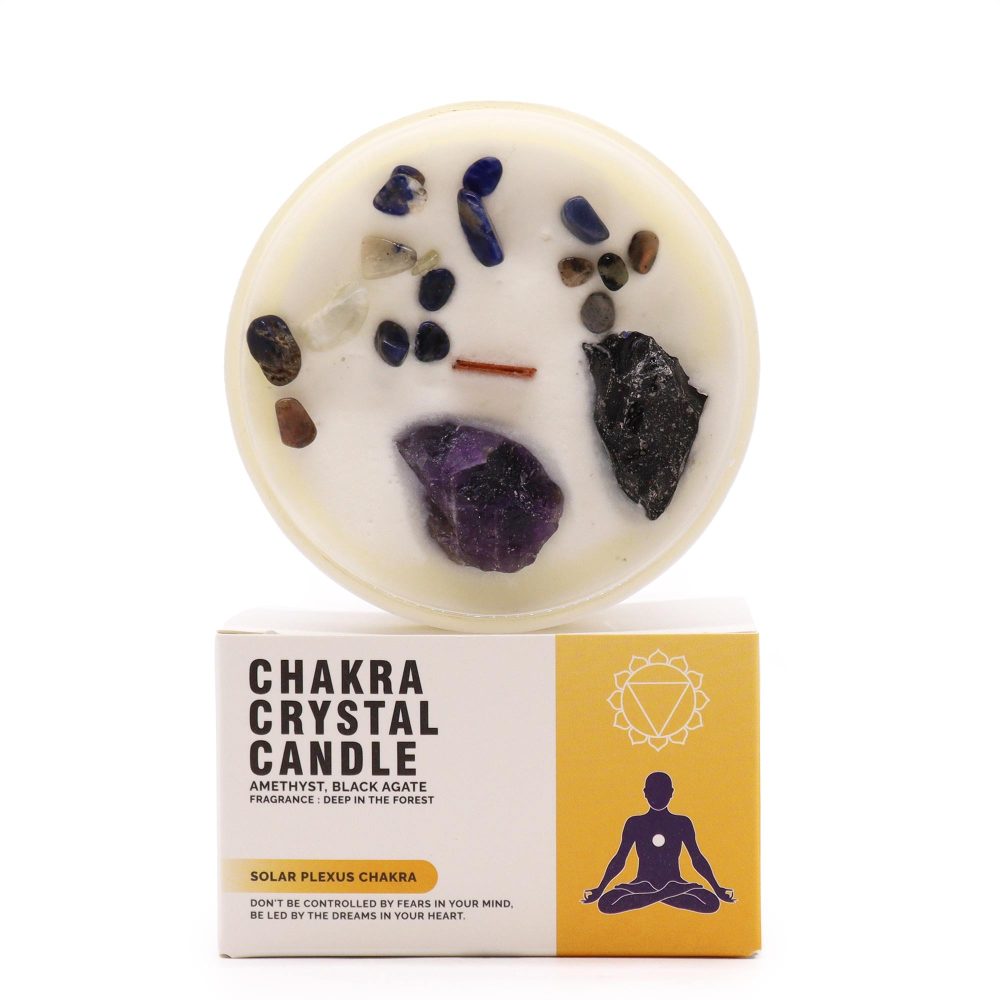 A crystal candle sits on top of its box, on a white surface. The wax of the candle is adorned with various gemstones. The box reads: "CHAKRA CRYSTAL CANDLE AMETHYST, BLACK AGATE FRAGRANCE: DEEP IN THE FOREST SOLAR PLEXUS CHAKRA DON'T BE CONTROLLED BY FEARS IN YOUR MIND. BE LED BY THE DREAMS IN YOUR HEART."