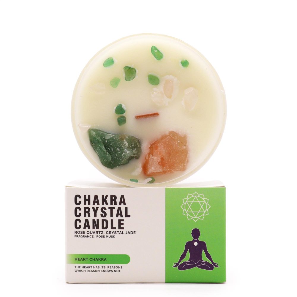 A chakra crystal candle sits atop its packaging. The packaging is white and green and features text that reads “CHAKRA CRYSTAL CANDLE ROSE QUARTZ, CRYSTAL JADE FRAGRANCE: ROSE MUSK HEART CHAKRA THE HEART HAS ITS REASONS WHICH REASON KNOWS NOT.”