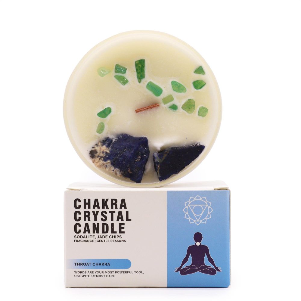 A white candle with green and blue crystals rests on a white box that reads "CHAKRA CRYSTAL CANDLE. SODALITE, JADE CHIPS. FRAGRANCE: GENTLE REASONS. THROAT CHAKRA. WORDS ARE YOUR MOST POWERFUL TOOL, USE WITH UTMOST CARE." The box also has an image of a person meditating.