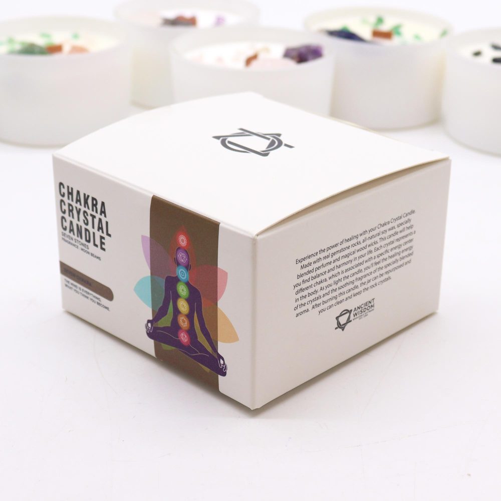 A Chakra Crystal Candle box sits prominently, bearing text: "CHAKRA CRYSTAL CANDLE SEVEN STONES FRAGRANCE - MOON BEANS" and promotional text about healing and gemstones. A yoga pose graphic adorns the box's side; blurred candles sit in the background.