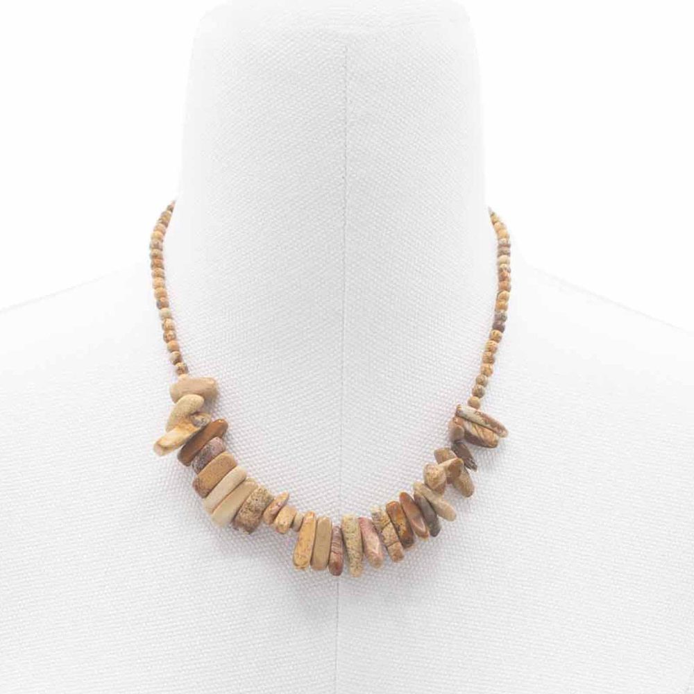 A necklace, crafted from brown and tan stone fragments and small beads, drapes against the pale form of a mannequin. The stones are centered in the front and the beads go around the back.