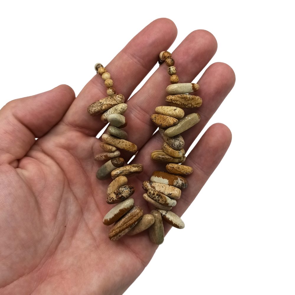 Two handmade earrings, constructed of stacked, elongated beads, rest in the palm of a human hand against a white background.