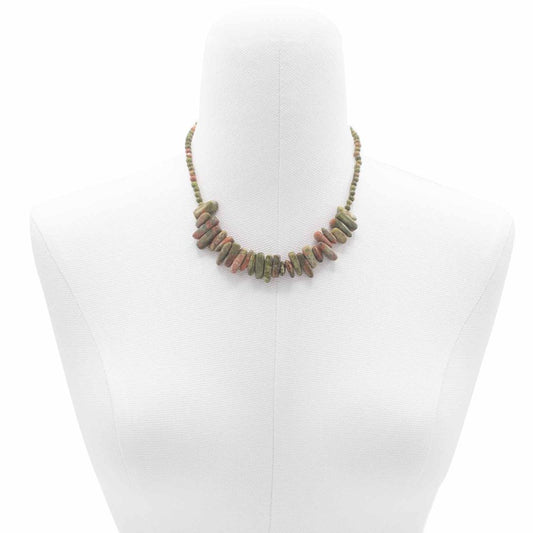 A necklace featuring oblong green and red beads is draped on a white, headless mannequin centered in the frame.