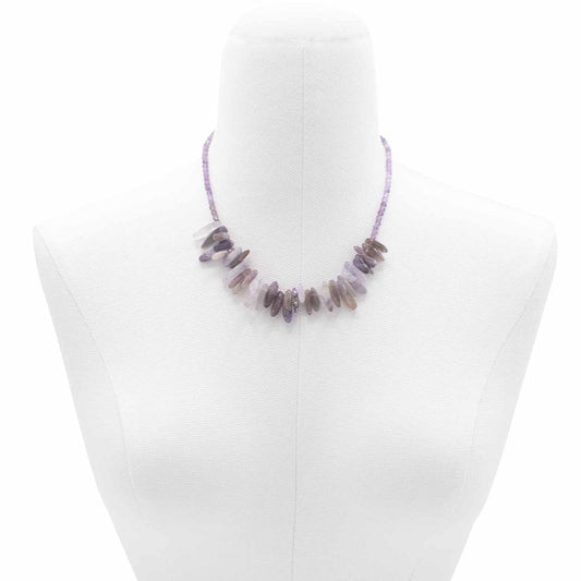 A purple, beaded necklace rests on a white mannequin. The necklace includes larger, irregular amethyst pieces spaced along the front.