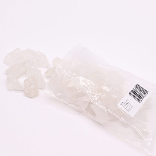 Clear quartz crystals spill from a plastic bag onto a white surface. The bag contains additional crystals and a label indicating "Rock Quartz," "Raw Crystals (500gm)," and origin as imported from China.