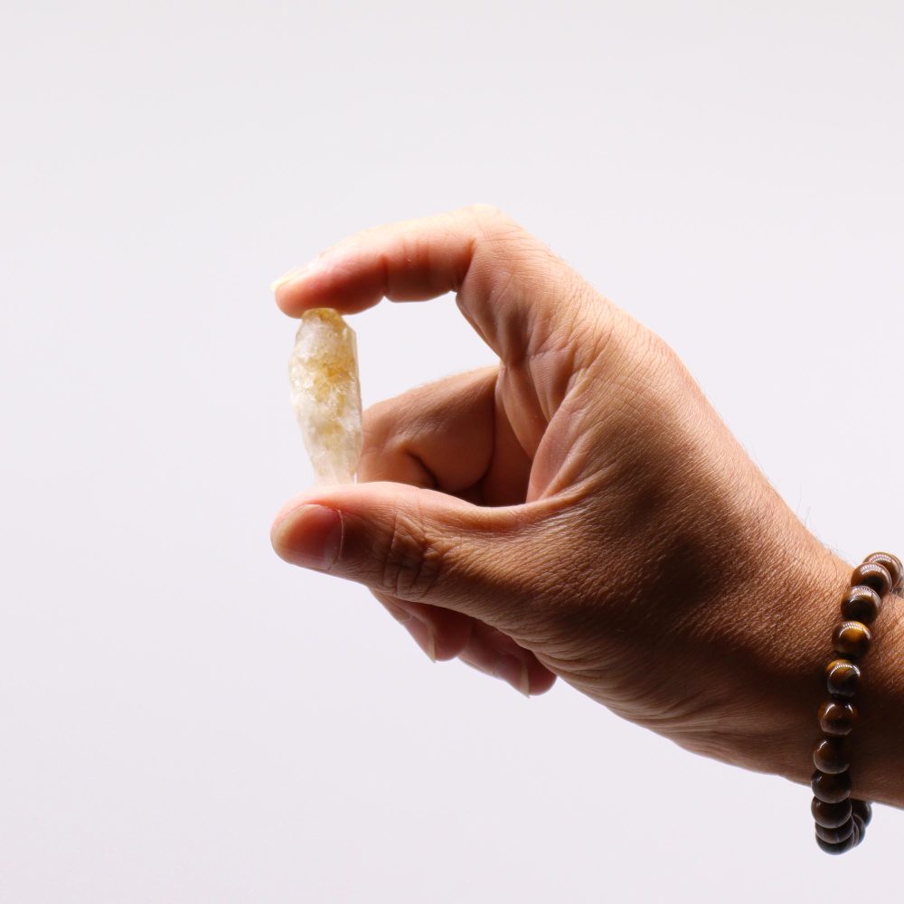 A hand holds a pale yellow, pointed crystal against a white background.