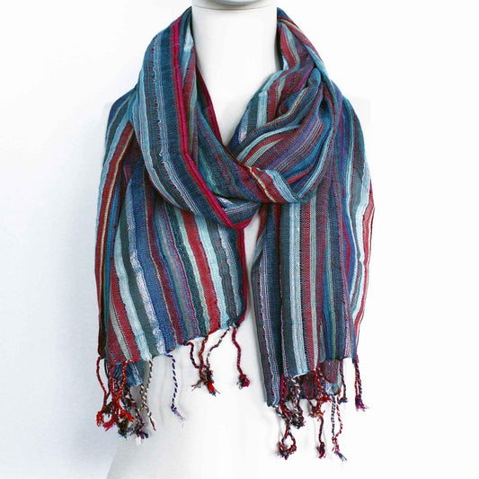 A striped scarf, folded and draped, displays various shades of blue, red, and gray on a mannequin against a white background.