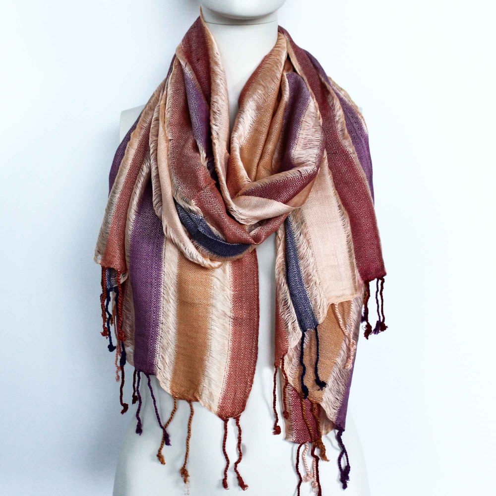 A striped scarf, draped around a mannequin, displays autumnal colors and textured fringes against a white background.