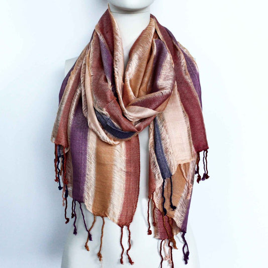 A striped scarf, draped around a mannequin, displays autumnal colors and textured fringes against a white background.