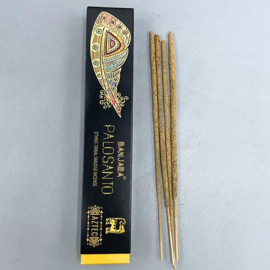 Box labeled "BANJARA® PALOSANTO Ethno Tribal Smudge Incense," featuring a colorful feather design, lies next to four incense sticks on a light gray surface. "AZTEC" is printed with tribal motifs.