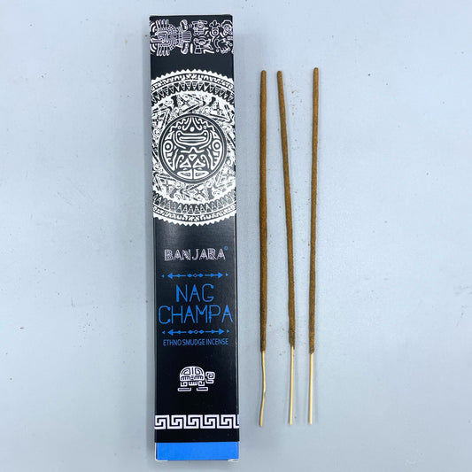 Incense sticks lie beside a black and blue box labeled "BANJARA NAG CHAMPA ETHNO SMUDGE INCENSE" with intricate white designs, set against a plain background.