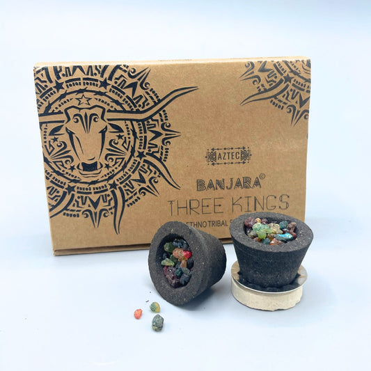Two black cone-shaped incense pieces with colorful resin chunks rest in front of a box featuring tribal art and text: "AZTEC BANJARA THREE KINGS ETHNO TRIBAL."
