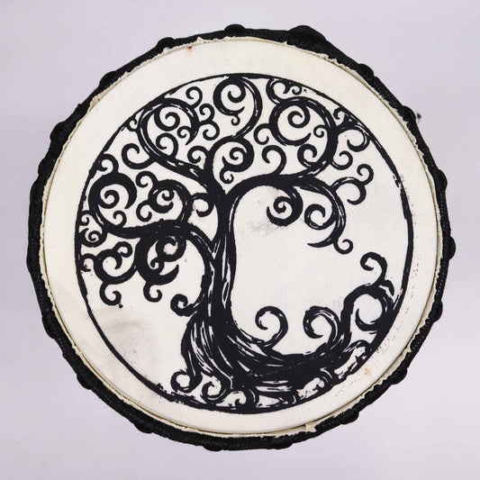 A circular, black outline encloses an intricate tree design with swirling branches. The tree is centered on a light background, resembling art on a round slice of wood.