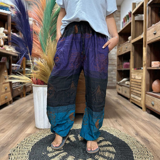 Multicolored patterned harem pants are being worn by a person standing on a woven rug inside a shop.