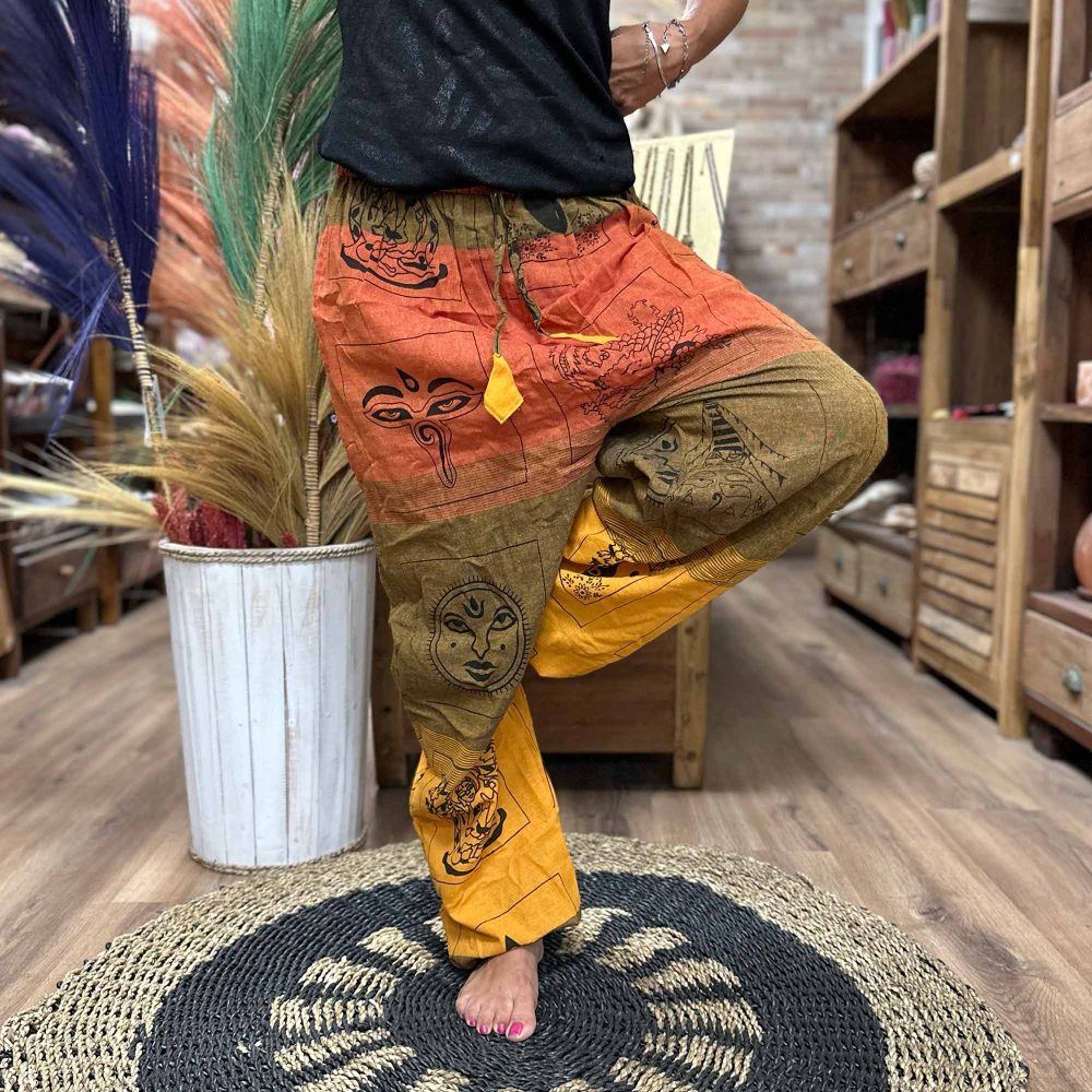 Printed pants stand on a woven mat. A person wearing them balances on one leg in a shop.