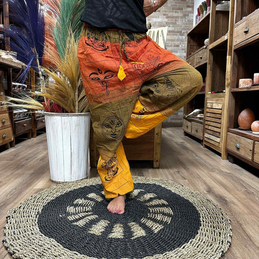 Printed harem pants are being modeled in a store.  The pants feature various designs including faces and symbols in orange, brown, and gold. The setting is a shop with wooden floors and shelves.