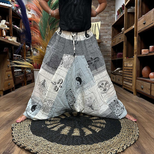 A person wearing patterned harem pants, featuring yin-yang symbols and other designs, stands on a round mat in a shop with wooden shelves.