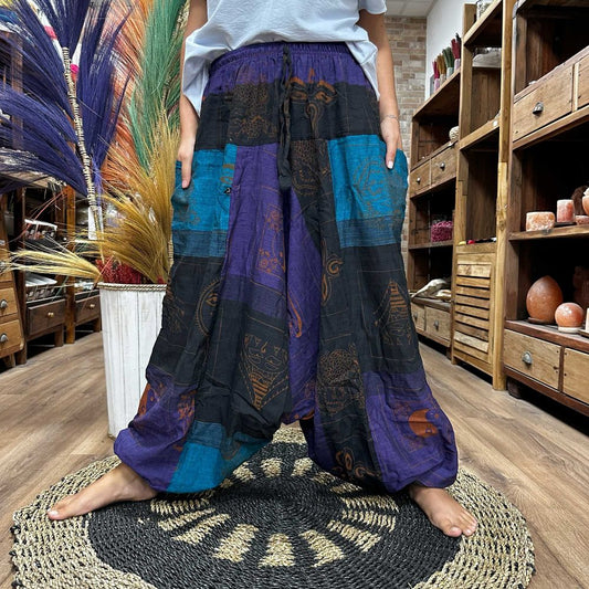 Patchwork harem pants, patterned with symbols, are worn by a person standing on a woven mat inside a shop.