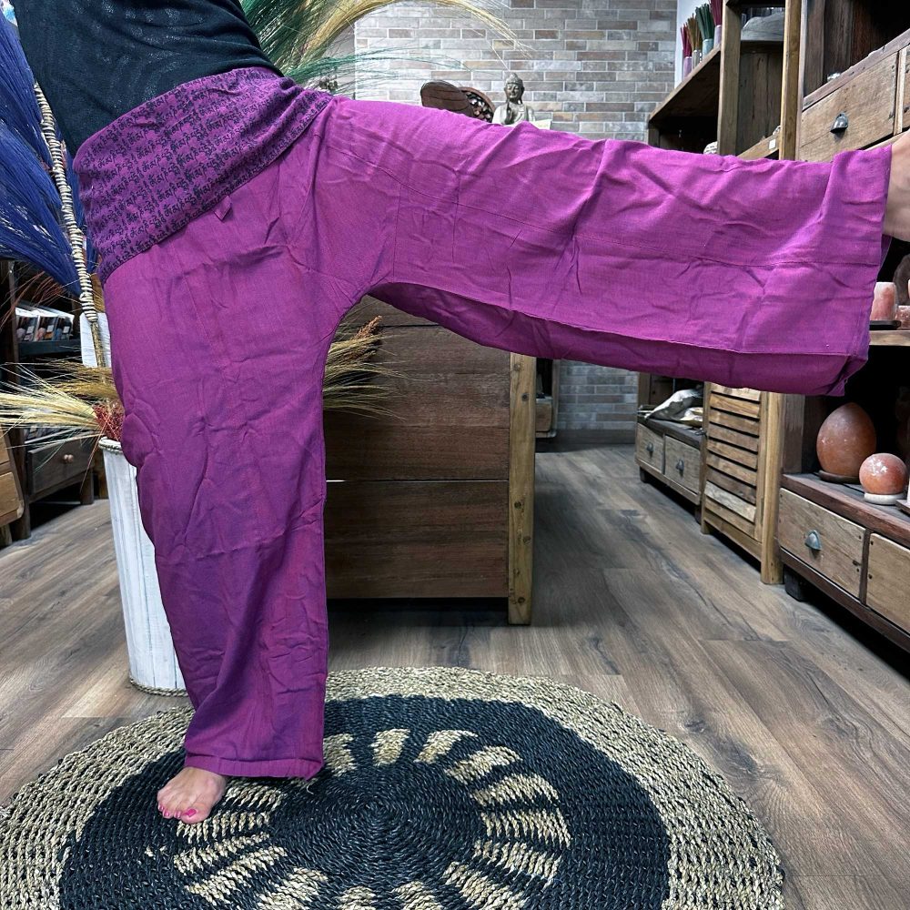 Purple Thai fisherman pants are being modeled in a shop. The pants have a dark waistband with indiscernible text. The setting is a wooden-floored store with wooden furniture.
