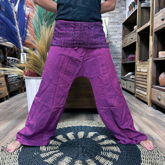 Purple harem pants, adorned with a waistband of printed text, are worn by a person standing on a circular rug inside a shop.