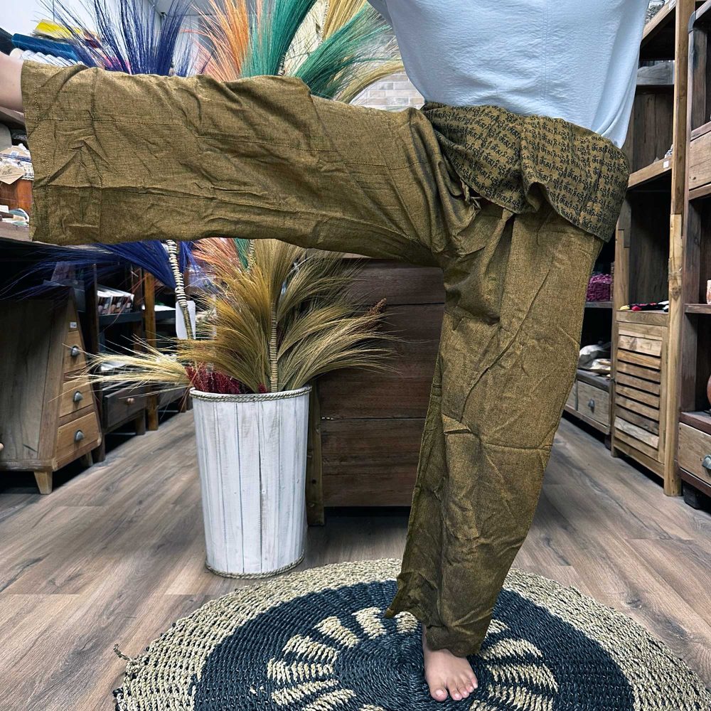 Olive-green Thai Fisherman pants are being modeled, showcasing their drape. The model stands on a circular rug in a shop with wooden furniture and dried flowers.