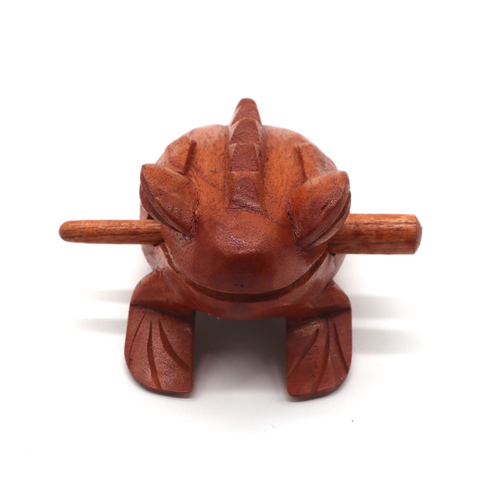 A wooden frog-shaped percussion instrument with a stick inserted, used for creating sounds; set against a plain white background.