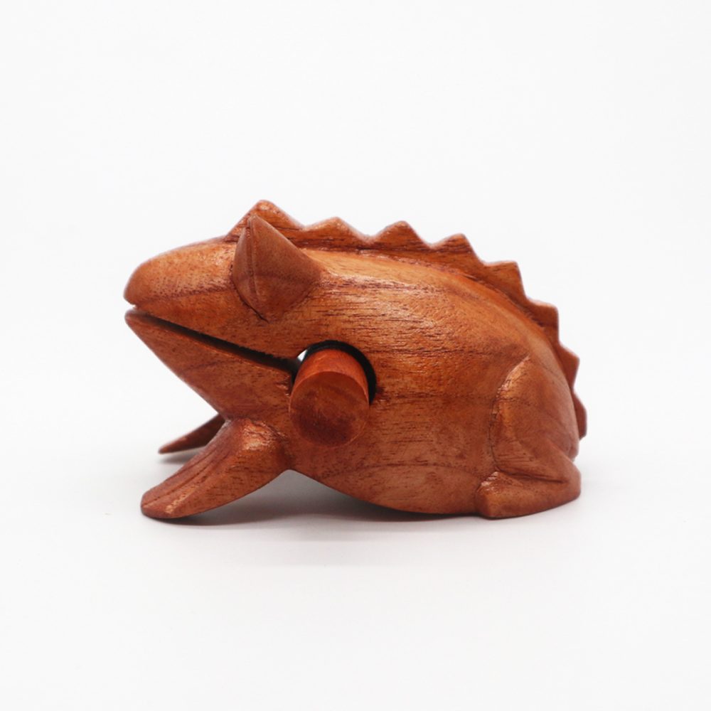 A carved wooden frog with a stick resting in its mouth is on a plain white background, depicting a sound-making instrument.