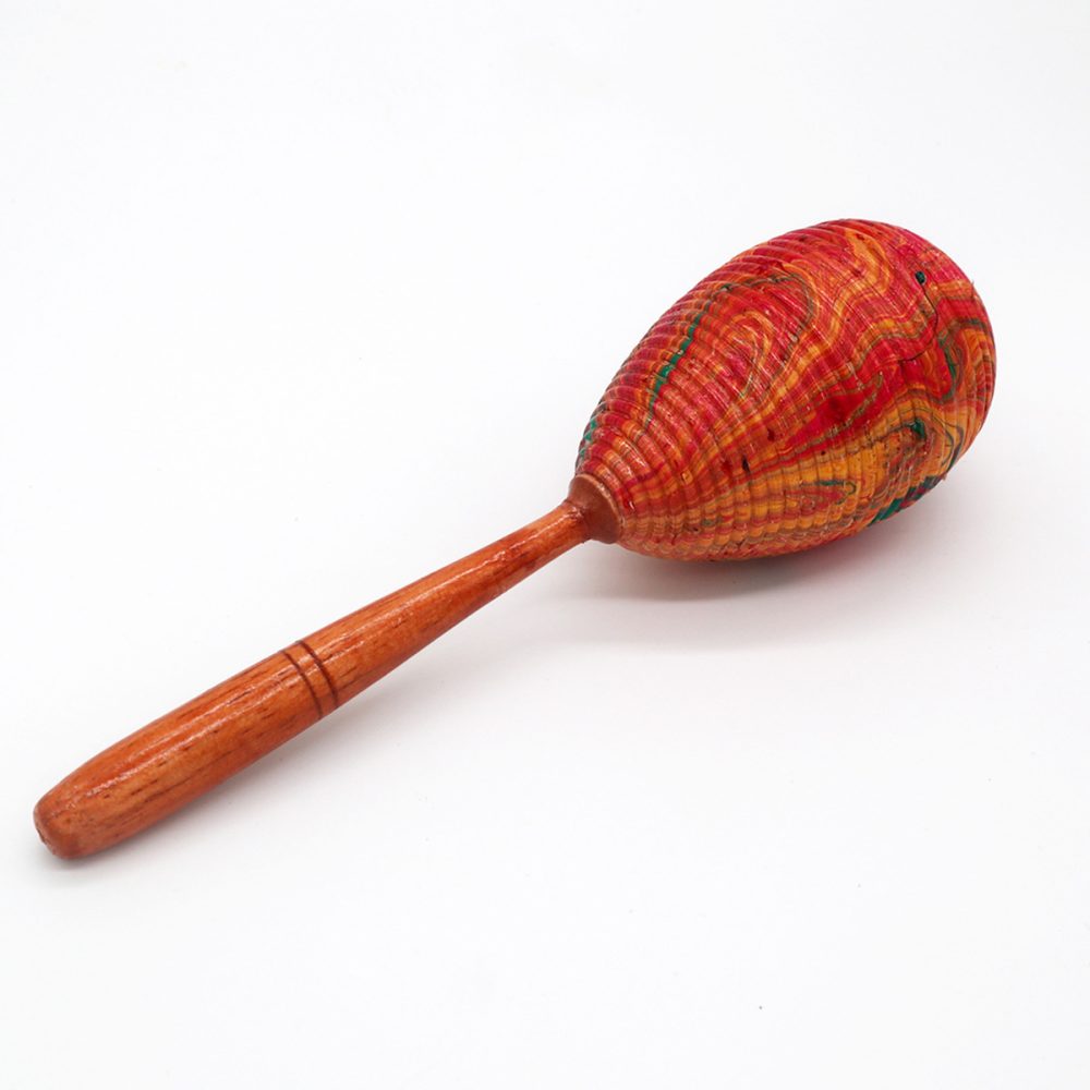 A colorful, textured maraca rests on a white surface. It features a vibrant red and orange spherical head attached to a smooth wooden handle.