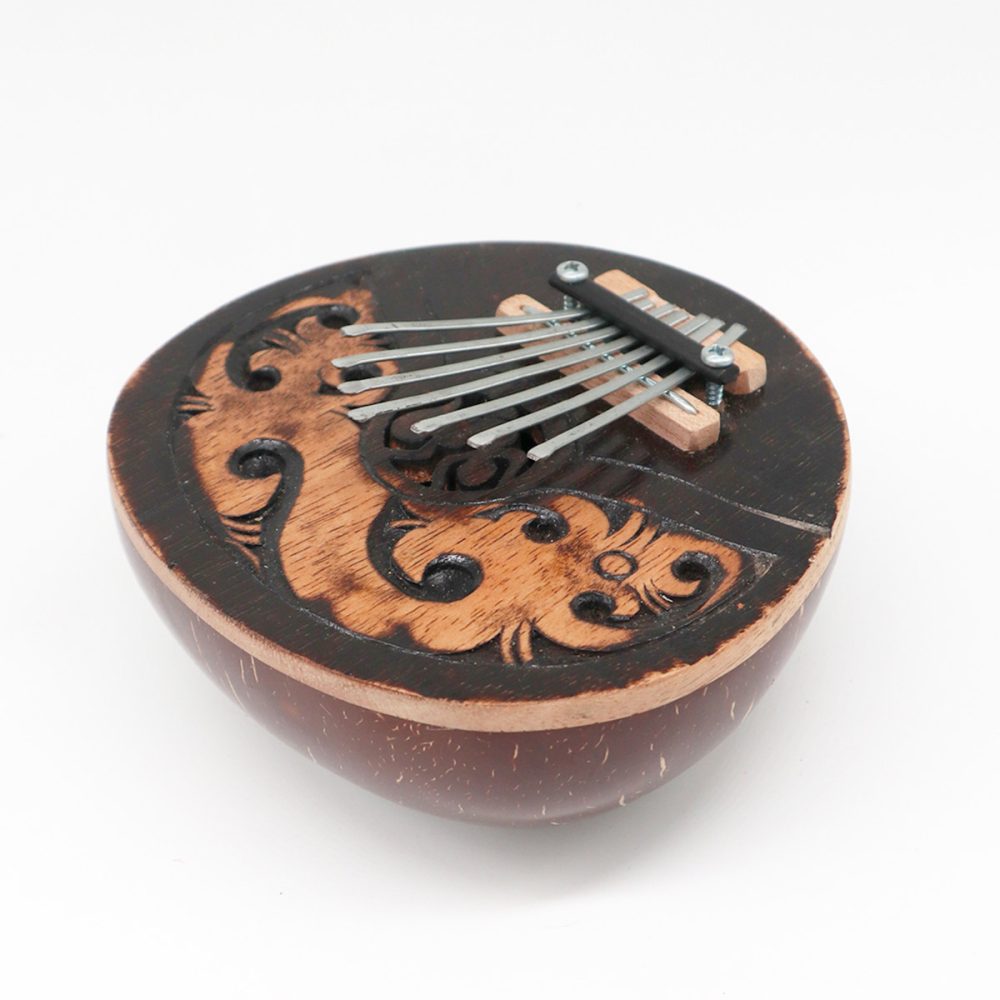 A small wooden kalimba with metal tines rests atop a decorated, carved design. It lies on a seamless white background, enhancing its intricate craftsmanship and smooth, rounded body.