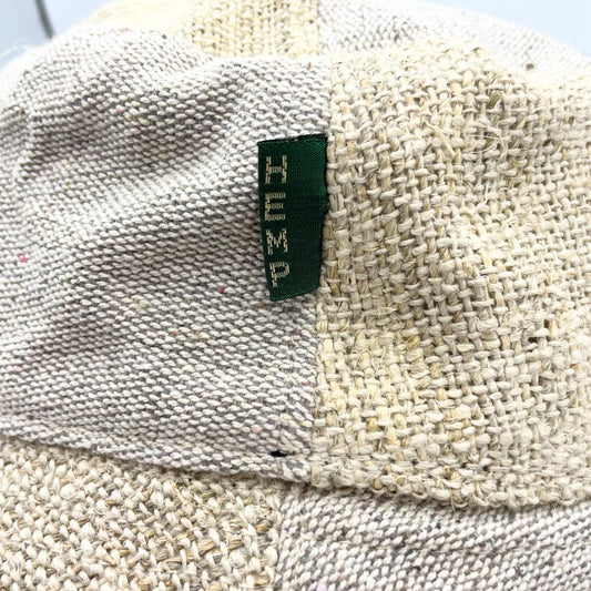 A hemp bucket hat displays a green label reading "HEMP". The off-white hat shows varied textures in its woven hemp fabric.
