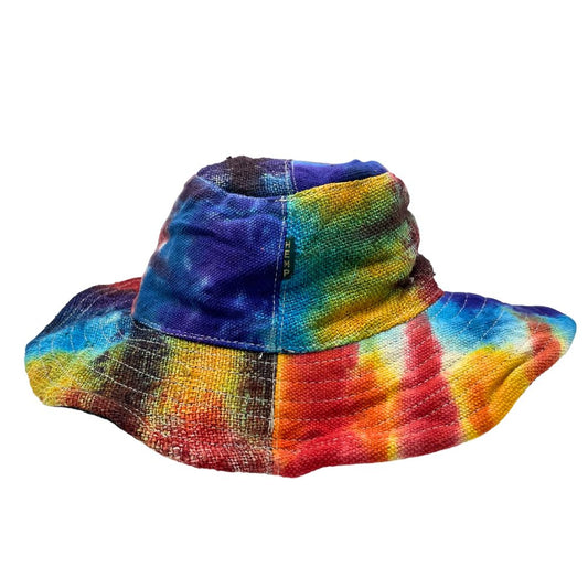 A hemp bucket hat, tie-dyed in vibrant rainbow colors, sits against a white background. The word "HEMP" is visible on the hat.