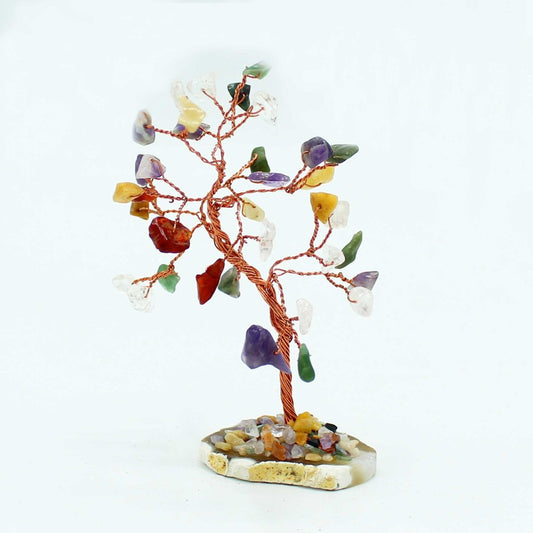 A copper wire tree sculpture, adorned with colorful gemstone leaves, stands on a small, irregularly shaped base of stones against a white background.