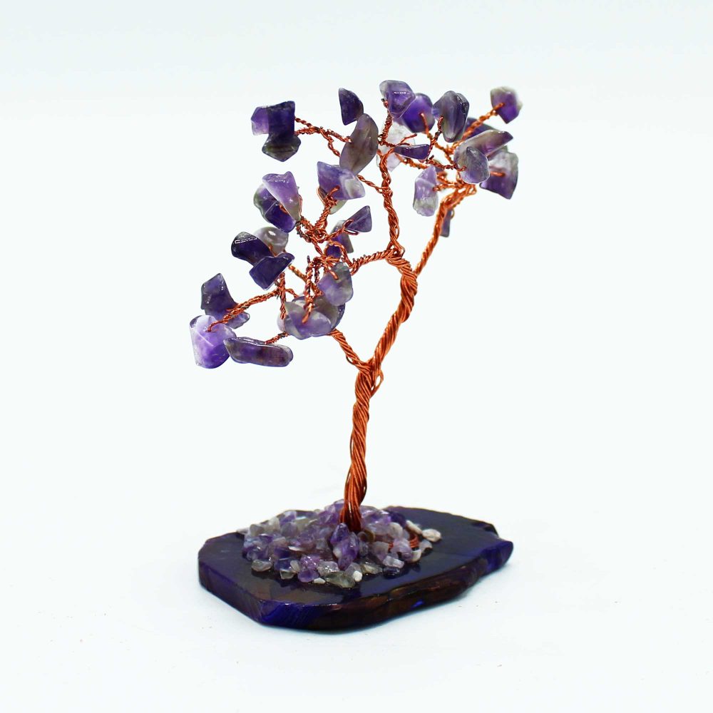 A copper wire tree, adorned with amethyst stones, stands on a dark purple agate base. Smaller amethyst pieces are scattered at its base.