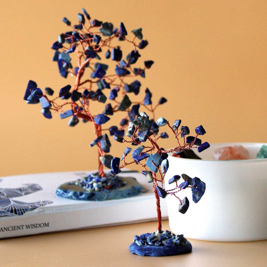 Two lapis lazuli stone trees, crafted with copper wire, stand on a book titled “ANCIENT WISDOM,” near a bowl.