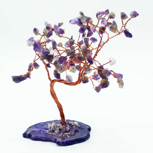 A copper-wire tree, adorned with purple amethyst stones, stands on a purple agate base against a white backdrop.