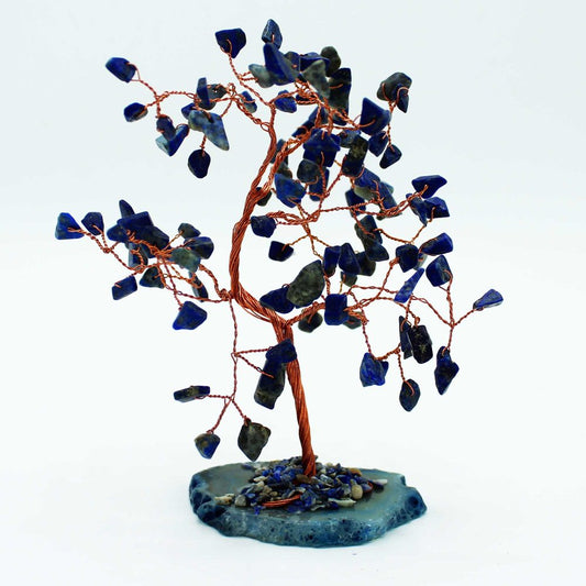 A lapis lazuli and copper wire tree stands on a blue stone base.  The tree's branches are adorned with small, dark blue stones. The background is white.