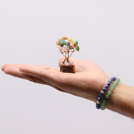 A miniature gemstone tree, crafted from wire and various colored stones, rests on a person's open palm.