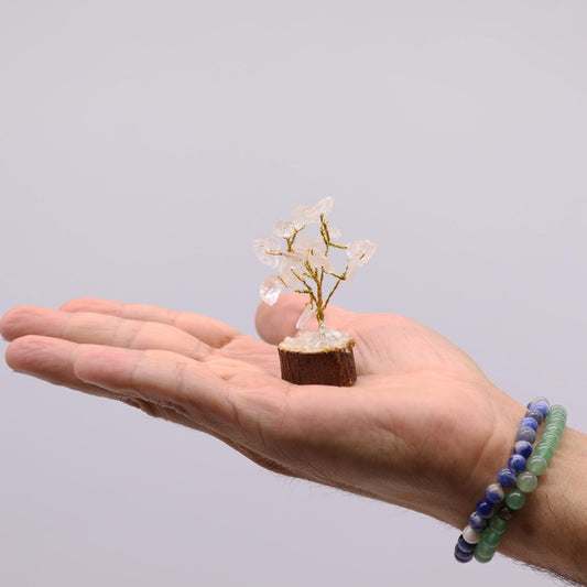 A small quartz crystal tree, crafted with gold wire, rests on a person's palm against a white background.
