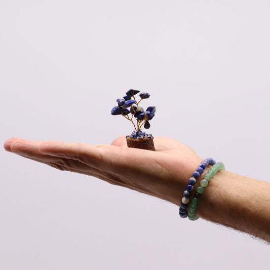 A miniature lapis lazuli tree rests in a hand,  adorned with wire branches. The hand also wears two beaded bracelets; one lapis lazuli and one green.